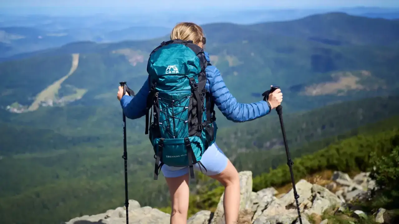 Kobieta z turkusowym plecakiem turystycznym i kijkami trekkingowymi na szczycie góry.