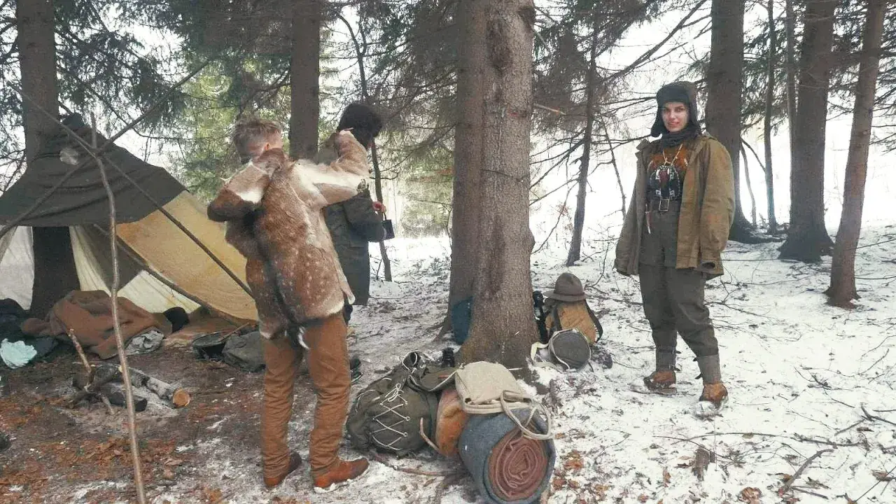 Zimowy obóz bushcraftowy. Dwie osoby w strojach z epoki, namiot, plecaki i sprzęt survivalowy.