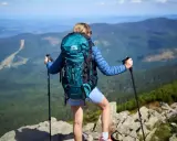 Kobieta z turkusowym plecakiem turystycznym i kijkami trekkingowymi na szczycie góry.