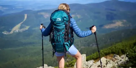 Kobieta z turkusowym plecakiem turystycznym i kijkami trekkingowymi na szczycie góry.