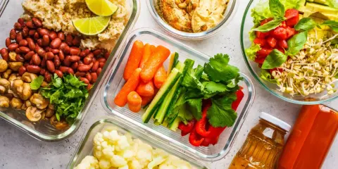 Gotowe pojemniki z jedzeniem na biwak bez gotowania: ryż z fasolą i pieczarkami, warzywa pokrojone w słupki, kalafior, sałatka z pomidorami i awokado, hummus i napoje.