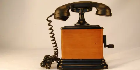 Stary telefon na korbkę z drewnianą obudową i czarną słuchawką.