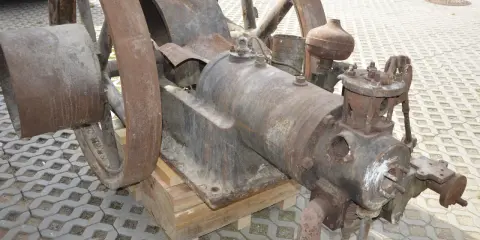 Zardzewiały silnik na gaz drzewny, z dużymi kołami, stoi na drewnianych klockach.