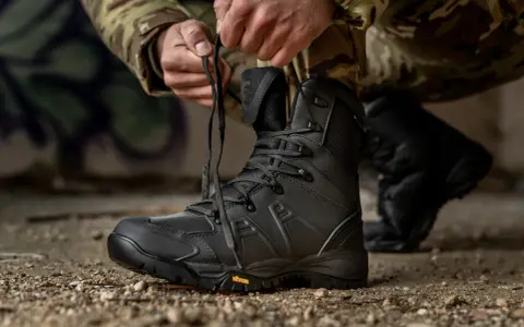 Mężczyzna w mundurze maskującym sznuruje czarne buty taktyczne. Gotowy na każde wyzwanie, te buty WOT zapewnią komfort i bezpieczeństwo.