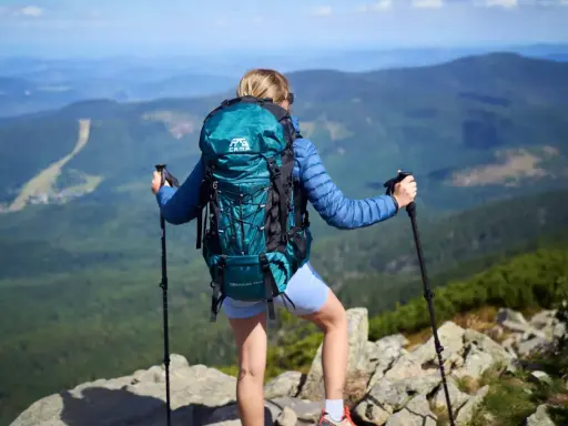 Kobieta z turkusowym plecakiem turystycznym i kijkami trekkingowymi na szczycie góry.