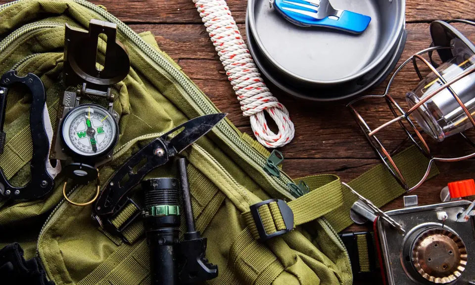 Gotowy **zestaw survivalowy**: plecak, kompas, nóż, latarka, krzesiwo, lina, kuchenka turystyczna, menażka i sztućce.