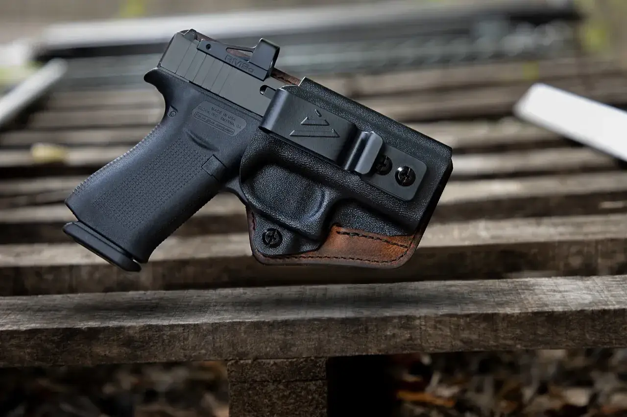 Pistolet Glock w czarnej kaburze z brązową skórzaną wstawką, gotowy do noszenia.