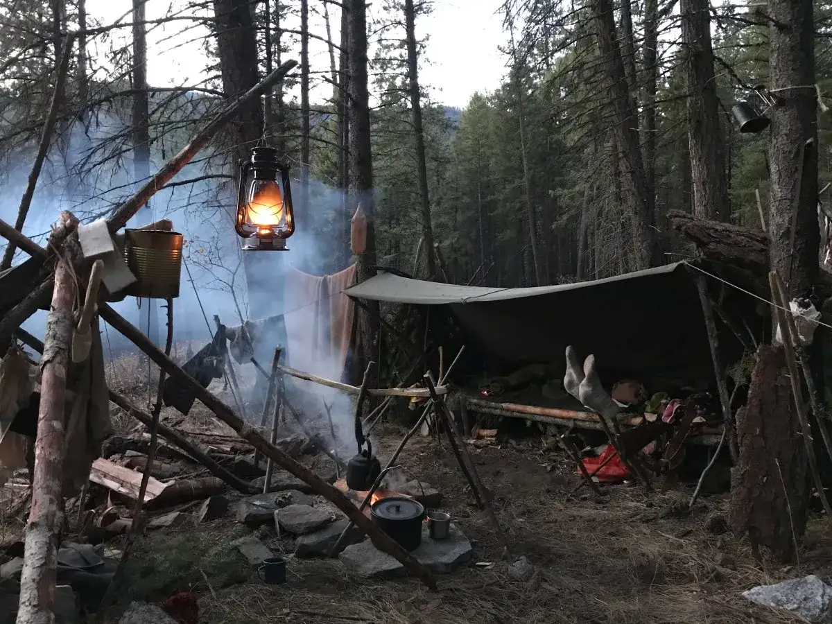 Ognisko i prowizoryczne schronienie w lesie, lampa naftowa oświetla dym. To prawdziwy bushcraft – sztuka przetrwania w dziczy.