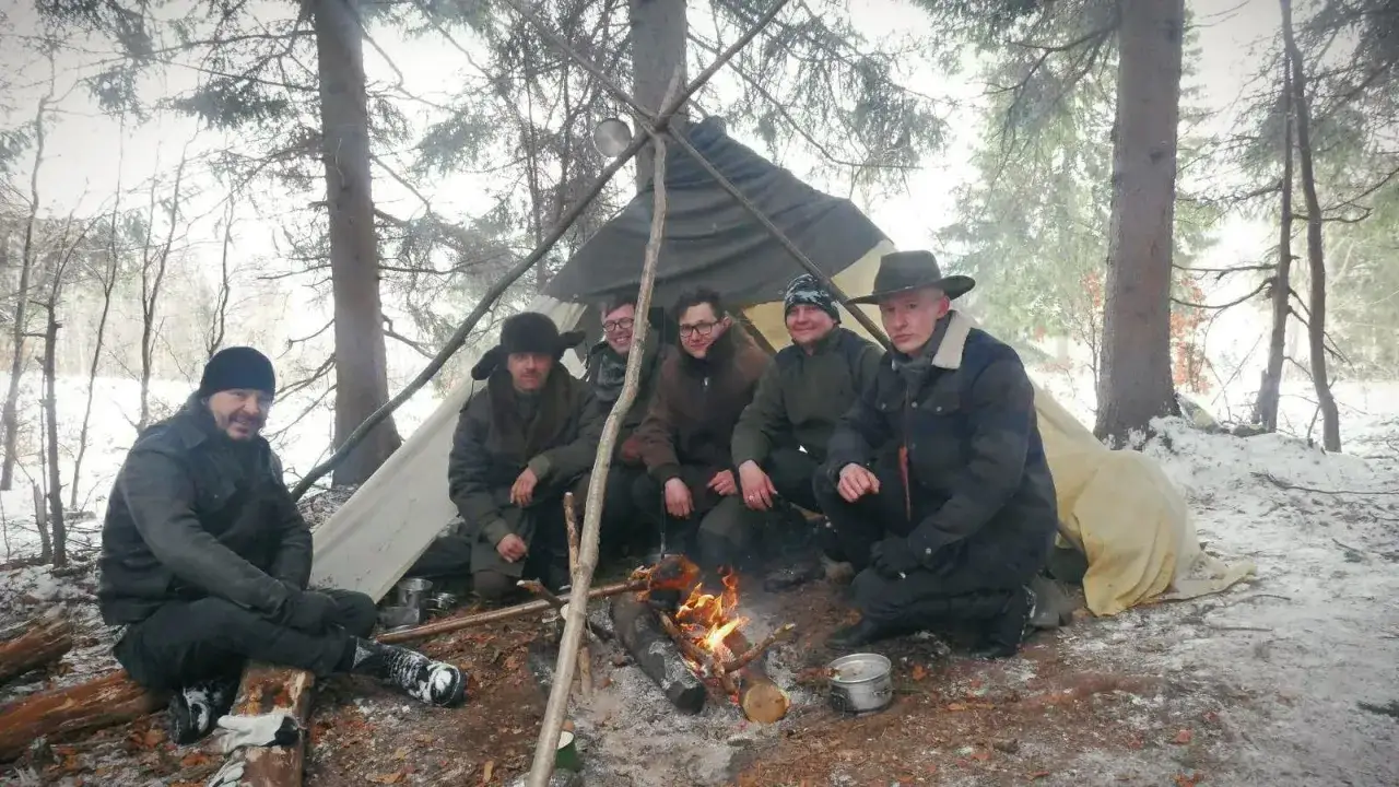 Grupa ludzi przy ognisku pod namiotem w lesie. To przykład, bushcraft co to znaczy – życie w zgodzie z naturą.