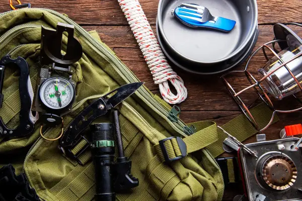 Gotowy **zestaw survivalowy**: plecak, kompas, nóż, latarka, krzesiwo, lina, kuchenka turystyczna, menażka i sztućce.