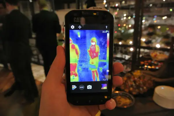 Ręka trzyma smartfon Cat S60 z włączoną termowizją, pokazującą dwie osoby w cieplejszych barwach.